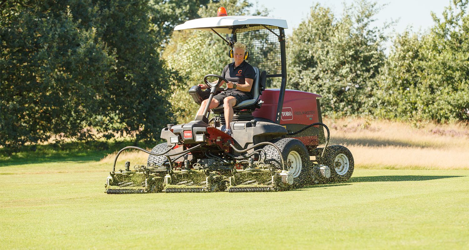 Greenkeeper op de maaimachine bezig op de golfbaan.